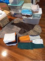 Photo showing folded bed linens in various colors stacked on plastic bins, with towels in front and a leopard print blanket.