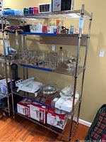 Front view of entire metal shelf showing five shelves with various glassware and kitchen items (contents not included).