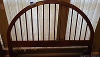 Front view of the queen size wooden headboard showing arched top and vertical slats in front of a window with sheer curtains.