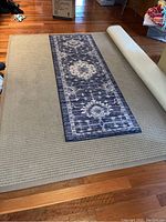 Photo of the large 8x10 beige Berber area rug with textured pattern and the navy blue floral patterned runner rug placed on top of it.