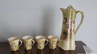 Photo of the antique Nippon chocolate pot and 4 matching cups showing full set and details of floral decoration.