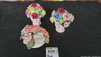 Three bone china floral arrangements, two in vases and one small cluster, displayed on a black surface with a Maxsold tag