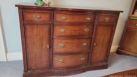 Front view of vintage solid wood buffet showing three central drawers with brass pulls and side cabinet doors.