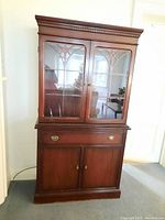 Front view of National Furniture cherry wood cabinet showing two glass doors with decorative wood framing, drawer, and base doors.
