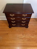 Front view of a wood chest of drawers with 4 drawers showing brass drawer handles and polished wood surface.