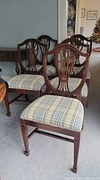 Set of five antique wooden dining chairs arranged with visible carved backs and plaid upholstered seats.