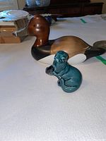 Wood carved red head duck and teal ceramic seal displayed on a white cloth background