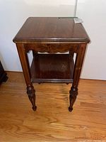 Full photo showing wood end table with one shelf and carved legs.