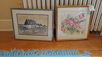 Two framed artworks side by side on floor, one watercolour of house, one floral watercolour
