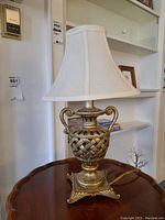 Full view of table lamp showing fabric shade and ornate metal base on wooden table.