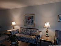 Room setting showing two brass base table lamps with fabric shades on either side of a floral patterned sofa.