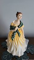 Front view of Royal Doulton Joan figurine with yellow dress and green plaid shawl
