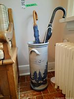 Front view of ceramic umbrella stand holding two umbrellas next to a radiator and bench.