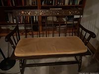 Front view of dark wood bench with curved armrests and carved floral design on backrest, seating cushion placed on bench seat.