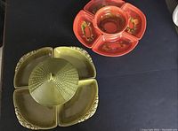 Two Mid-Century Modern ceramic serving sets, one olive green with four sectioned trays and central lidded compartment, the other orange-red with five trays and painted vegetable motifs.