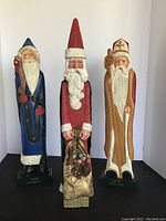 Front view of three Santa Claus figurines showing detailed painted features and inscriptions on bases.