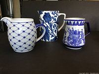 Front view of three blue and white pitchers showing floral, lattice, and landscape designs.