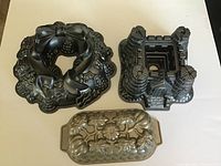 Three Nordicware cake pans: holiday wreath, castle, and fall loaf pan, displayed on white surface
