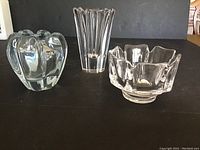 Three Orrefors crystal vases with different shapes and heights shown together on black surface.