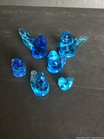 Front view of 6 blue glass bird figurines on a dark surface.