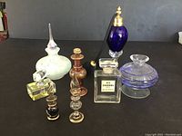 Photo showing front view of all 8 unique empty vintage perfume bottles with different colors, shapes, and stoppers including the blue atomizer and Chanel No. 5 bottle.