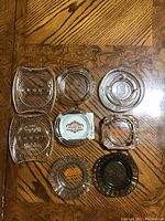 Top down view of 8 assorted vintage hotel and motel glass ashtrays on a wooden surface