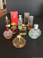 Nine assorted perfume bottles, some with visible Elizabeth Arden branding and original red box, arranged on black surface.