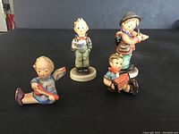 Front view of 4 Hummel musical figurines on black surface showing details and colors.