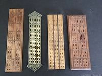 Four cribbage boards laid flat on a dark surface including brass and wooden boards with visible hole scoring tracks.