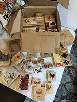 Top view of a box filled with various wooden rubber stamps and some outside arranged on the table, displaying multiple illustrated designs.