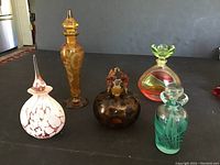Full view of all five decorative perfume bottles arranged on black surface showing variety of colors and designs