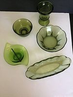 Five green glass dishes and serving pieces arranged on white surface, showing shapes and glass tone.