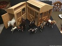 Shows the wooden stable with all horses in front, highlights open doors and stable size