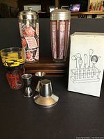 Full view of cocktail shakers, glasses, measure pourers, funnel, and boxed bar tools.