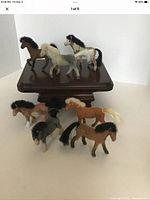 Seven vintage Breyer flocked horses and ponies displayed on a small wooden pedestal and flat surface, showing various poses and colors.