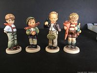 Four vintage M.I. Hummel boy figurines front view showing details of faces, clothing, and bases.
