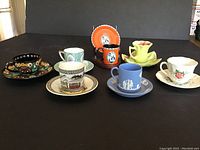 Photo showing all seven demitasse cups and saucers in a lineup, highlighting variety of colors and styles.