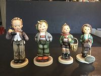 Front view of four Hummel figurines arranged in a row showing detailed color and size differences