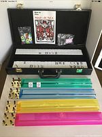 Full view of Mahjong set opened inside black leatherette carrying case with tiles, scoring racks, dice, chips, and instruction booklet displayed.