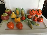 Photo showing the full set of 15 vintage anthropomorphic fruit and vegetable salt and pepper shakers arranged on a tray, including apples, pears, corn, oranges, pumpkins, strawberries, and tomatoes.