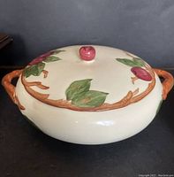 Front view of the vintage covered dish showing apple and leaf decoration with branch-shaped handles and apple knob on lid.