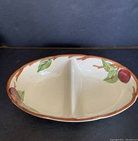Top view of oval divided dish showing apple and leaf patterns along the edges and dividing partition in the center.