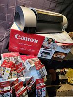 Canon printer on original box surrounded by unopened Canon ink cartridge boxes.