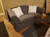 Loveseat fully covered with dark gray fitted cover, two cream pillows on it.
