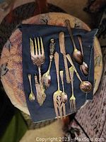 Top view of all 13 silver and silver plate serving pieces arranged on a dark cloth showing range of flatware types and designs
