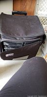Black rolling craft case closed with transparent front organizer pockets and handle on top