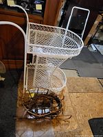 Side view of vintage white wrought iron tea cart with two lattice shelves and scrollwork details, rustic twig sled placed on floor in front
