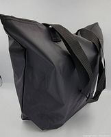 Side profile of a black nylon tote bag showing the smooth nylon fabric and wide black shoulder straps.