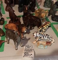 Various animal figurines including a glazed ceramic lion, a wooden elephant, ceramic donkey marked W Goebel Germany, white tiger porcelain, and other wild animal figures.