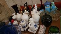 Photo of assorted vintage Avon perfume bottles, ceramic cups with blue floral designs, and multiple glass and ceramic jars on a wooden surface.